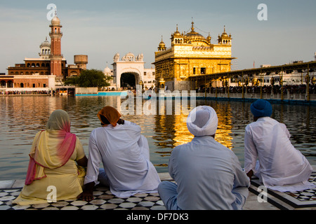Sikh pilgrims sitting in front of the Harmandir Sahib or Golden Temple, Amritsar, Punjab, India Stock Photo