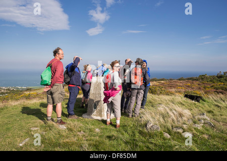 Group of Ramblers looking at view from trig point on Mynydd Eilian summit near Penysarn, Amlwch, Anglesey, North Wales, UK, Britain Stock Photo