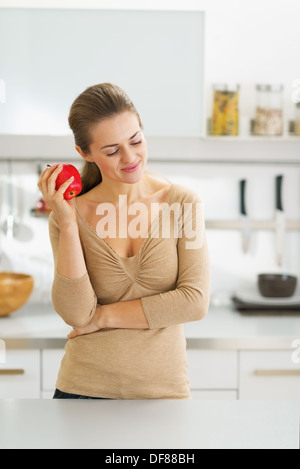 Thoughtful young housewife with apple in modern kitchen Stock Photo