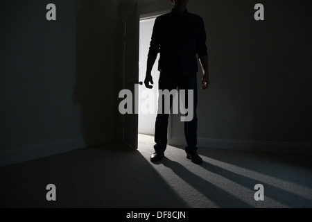 Silhouette of a male adult standing in an open doorway, entering a dark room. Model released Stock Photo