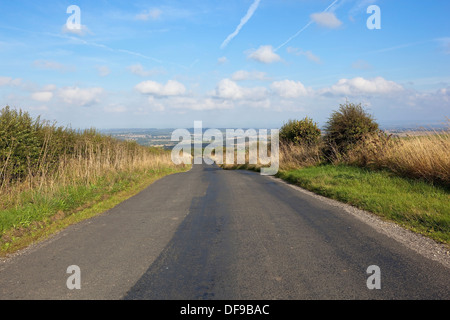 A country road going downhill towards a beautiful view of the Yorkshire wolds england under a blue sky in summer Stock Photo