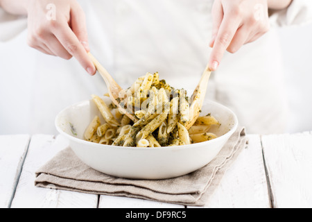 Cook's hands mixing traditionally made pesto in a white dish on a white table, holding wooden tools Stock Photo