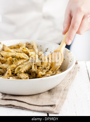 Cook's hands mixing traditionally made pesto in a white dish on a white table, holding wooden tools Stock Photo
