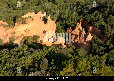 AERIAL VIEW. Ocherous hoodoos in sharp contrast with the surrounding green foliage. Rustrel, Lubéron, Vaucluse, Provence, France. Stock Photo