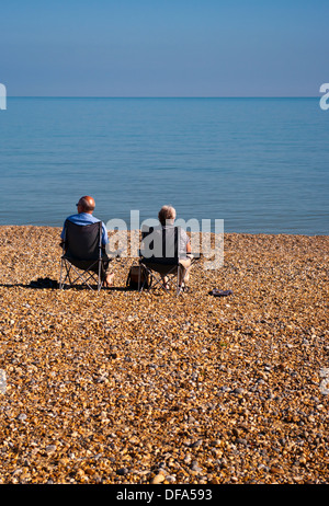 Rear View Of An Elderly Couple Sitting On Beach Chairs Looking Out To Sea Stock Photo