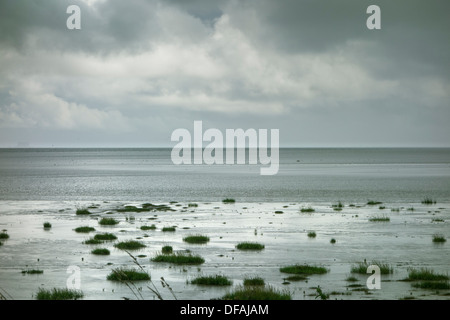 Dark grey stormy clouds, over an incoming tide. Stock Photo