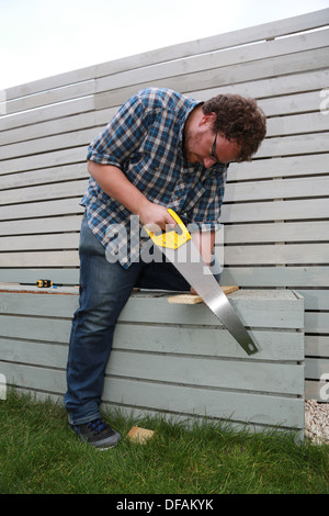 A man sawing a plank of wood outside. Stock Photo