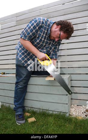 A man sawing a plank of wood outside. Stock Photo