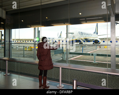 Stansted Airport, UK - March 7, 2012: Young woman looking trough the window at the Ryanair Terminal in the Stansted Airport Stock Photo