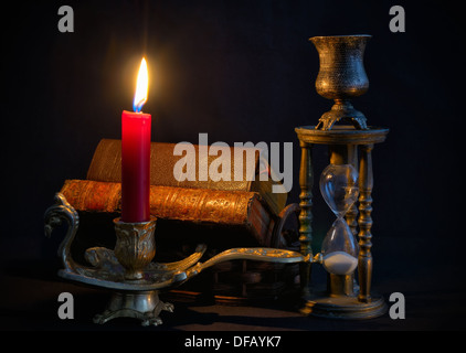 Vintage candlestick with red candle, books and hourglass in dark room Stock Photo