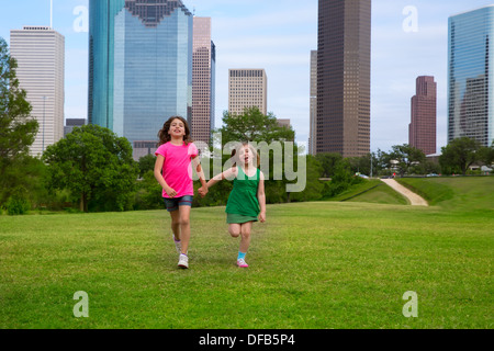 Two sister girls friends running holding hand in urban modern skyline on grass lawn Stock Photo