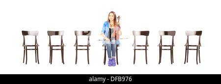 Casual young woman seated on a wooden chair holding a violin and waiting for job interview Stock Photo