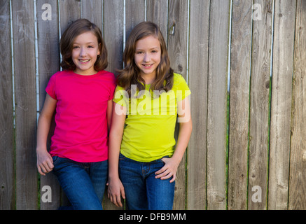 Twin sister girls with different hairstyle posing on wood backyard fence Stock Photo