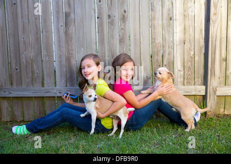 Twin sister girls playing with smartphone and chihuahua dog sitting on backyard Stock Photo
