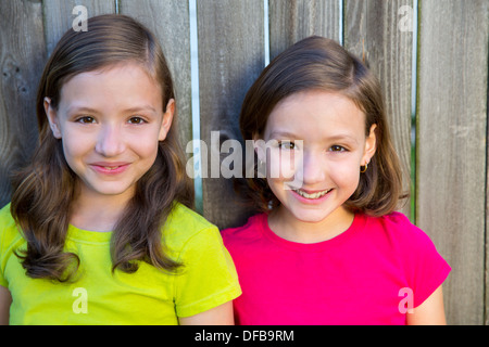 Happy twin sisters with different hairstyle smiling on wood backyard fence Stock Photo