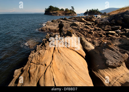 Long sandstone formation leading to a number of small rocky islands with man in the middle back to viewer Stock Photo