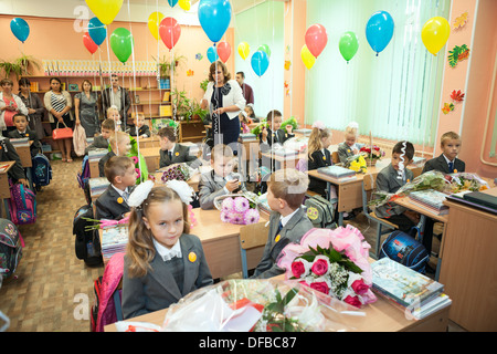 Small students sitting in decorated classroom at the first lesson in Russian elementary school, Russia. Parents standing behind Stock Photo