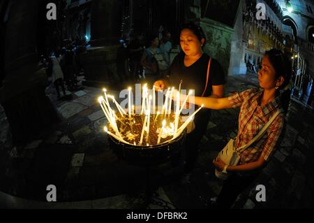Two Christians from Asia light candles before visiting the most important site of the Church of the Holy Sepulchre is the Aedicule (Holy Grave, Grave Chapel), the supposed location of Jesus' grave and the 14th station of the Via Dolorosa, that is visited by thousands of pilgrims and tourists daily, in Jerusalem, Israel, 12 September 2013. The Via Dolorosa (Way of Suffering) is a street in the old town of Jerusalem named after the path Jesus of Nazareth walked to his crucification. Jesus carried the cross, on which he later died via that road from the Antonia Fortress, then seat of Pilate, to G Stock Photo