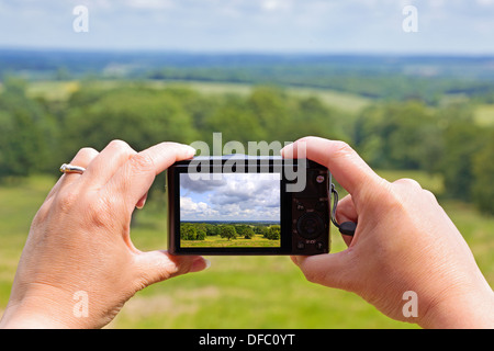 A woman using the rear lcd screen to compose and take a landscape photo with her compact digital camera using liveview. Stock Photo