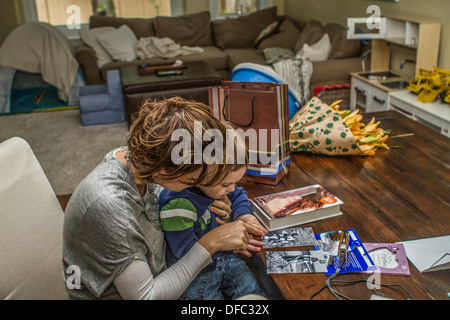 Mother with her arm around 3 year old son, sitting on her lap, looking thru pictures . Stock Photo