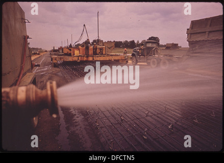 This image captures the construction of I-55 north of Durant, where water is being sprayed on the roadway base and steel rods to prepare the roadbed. The use of steel rods in road construction highlights the techniques used for reinforcing pavement structures. Stock Photo