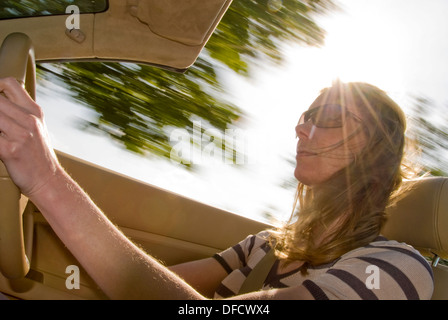 Pretty young woman, driving open topped sports car on a sunny day, with wind in her hair. Stock Photo