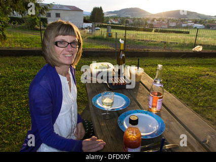 2 Aug 2013, Siaugues-St-Romain, Auvergne, France: woman sitting smiling on a wooden bench with simple meal cooked on a griddle Stock Photo