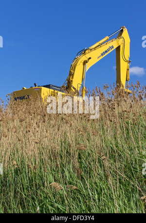 Yellow excavator silhouette on grassy hill against blue sky Stock Photo