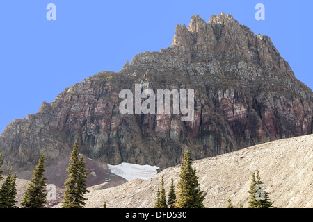 This image of Mount Reynolds at Glacier National Park shows purple rock face and remnants of a snow field. Stock Photo