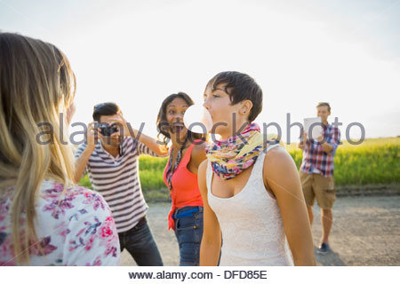 Cheerful friends looking at woman blowing bubble gum