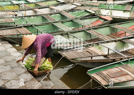 old woman with vegetables and boats docked on the Tam Coc River in Ninh Binh, Vietnam Stock Photo