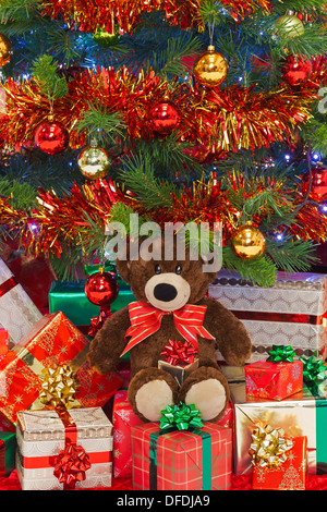 A handmade teddy bear wearing a bow in amongst gifts under a Christmas tree. Stock Photo