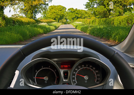 View from behind the steering wheel of a car whilst driving down a country road. Stock Photo