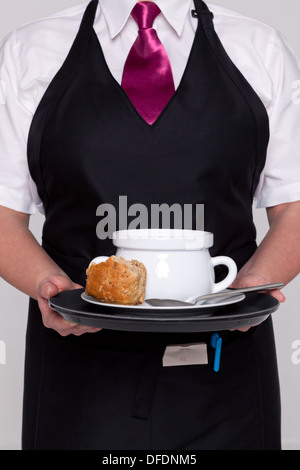 A waitress wearing an apron and tie serving a bowl of hot soup and fresh bread. Stock Photo