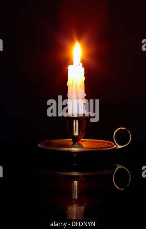 A single burning candle in a brass holder known as a chamberstick, against a black background. Stock Photo