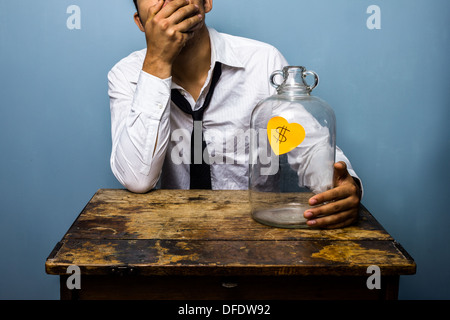Sad young businessman has spent all the money in his piggy bank Stock Photo