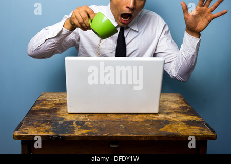 Clumsy young businessman is spilling coffee on his laptop computer Stock Photo