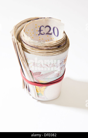 A roll of British notes held together by an elastic band with a plain background. Stock Photo