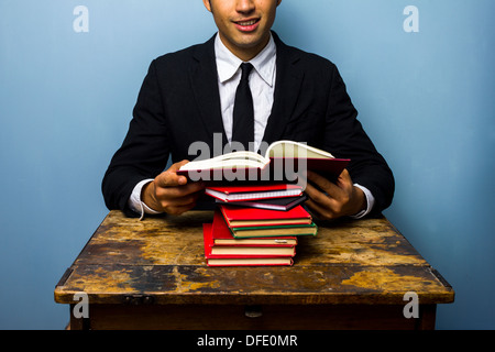 Young businessman is sitting at an old desk and reading a bunch of books Stock Photo