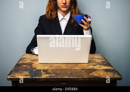 Young business woman is sitting at an old desk and working on her laptop whilst drinking coffee Stock Photo