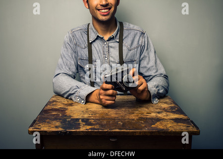 Young man with vintage camera is sitting at an old wooden desk Stock Photo