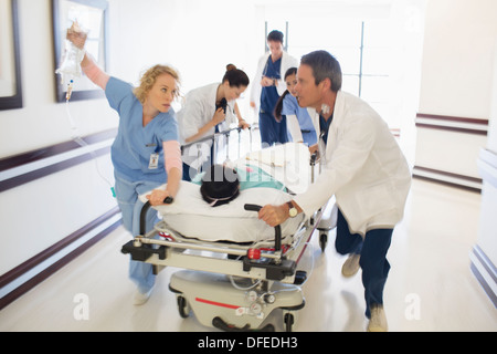 Doctors rushing patient on gurney in hospital corridor Stock Photo