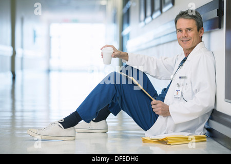 Portrait of smiling doctor drinking coffee on floor in hospital corridor Stock Photo