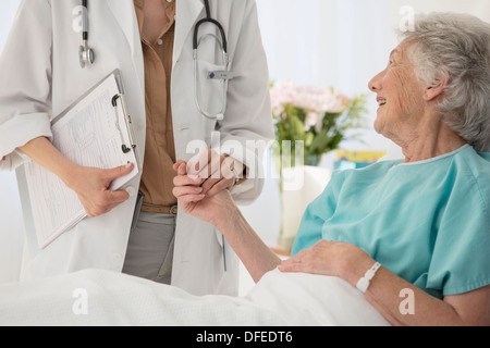 Doctor and aging patient holding hands in hospital Stock Photo