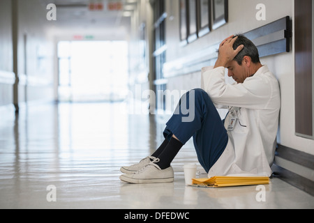 Doctor sitting on floor in hospital corridor with head in hands Stock Photo