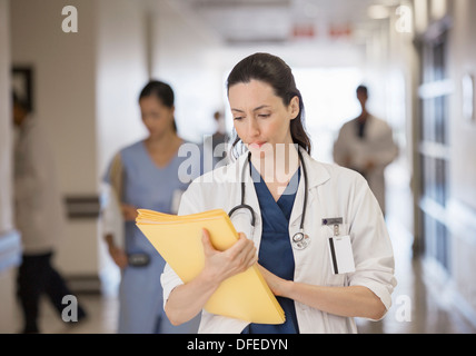 Doctor looking down at folder in hospital corridor Stock Photo