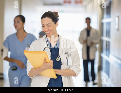 Doctor looking down at files in hospital corridor Stock Photo