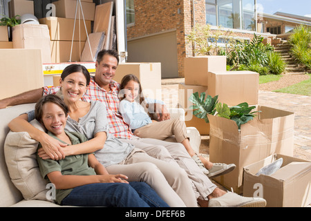 Portrait of smiling family sitting on sofa near moving van in driveway Stock Photo