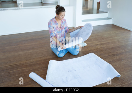 Woman examining blueprints on floor in empty living room Stock Photo
