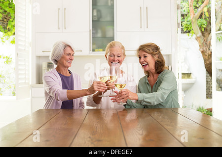 Senior women toasting wine glasses in kitchen Stock Photo